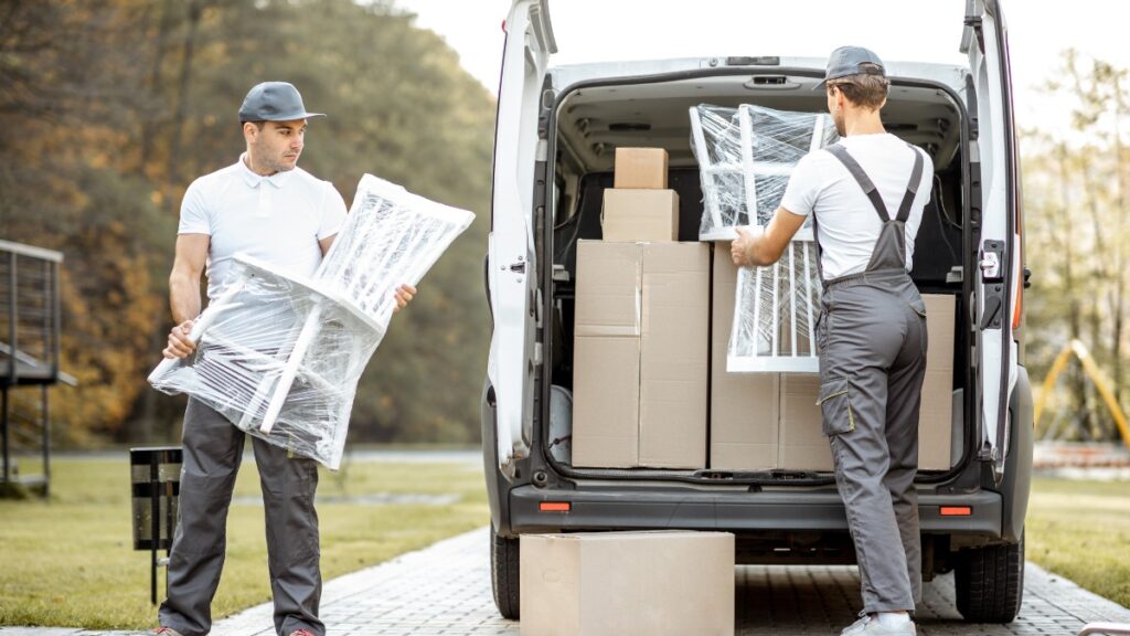 Two movers loading plastic-wrapped white chairs