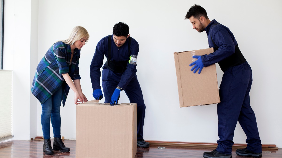 Two movers in blue uniforms packing and carrying cardboard boxes